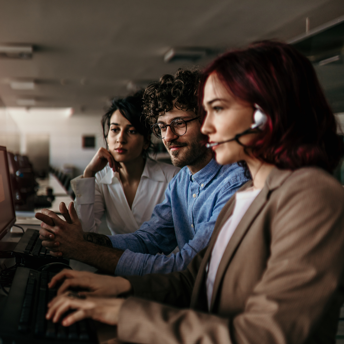 three people sitting in office room looking at project on computer